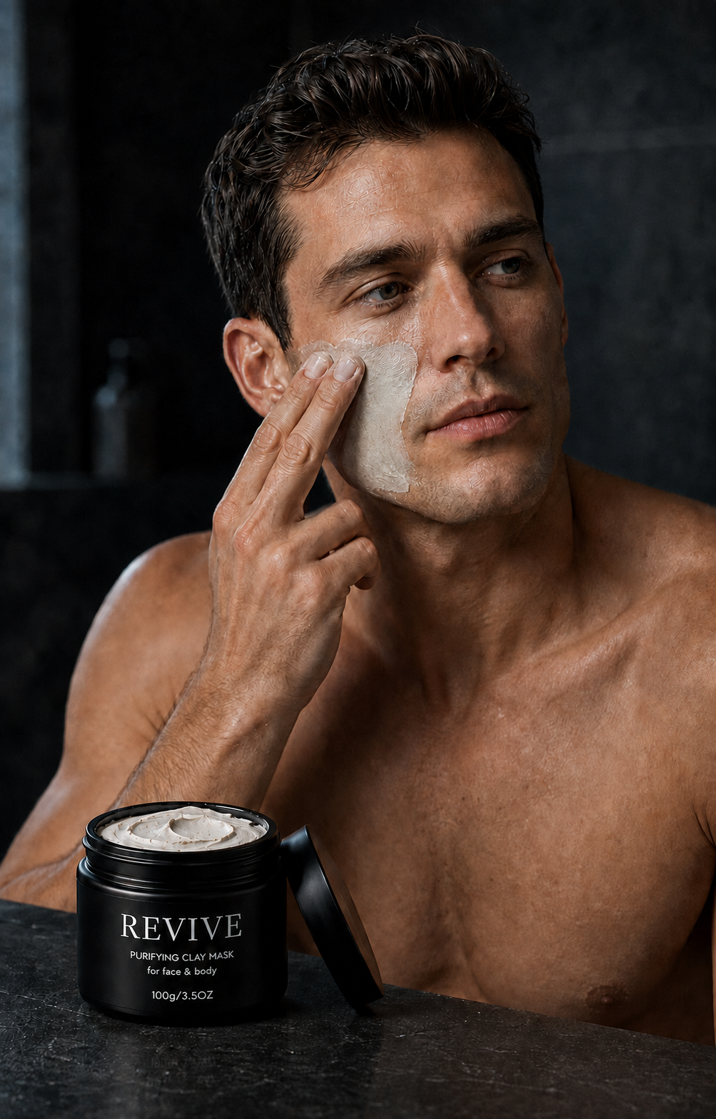 Man applying REVIVE Purifying Clay Mask to his cheek in a dark bathroom, with the open jar in the foreground